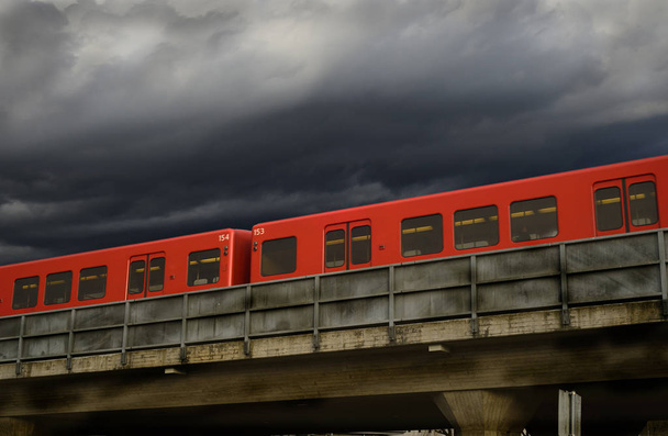 red subway cars on a concrete overpass against a dramatic sky - Φωτογραφία, εικόνα