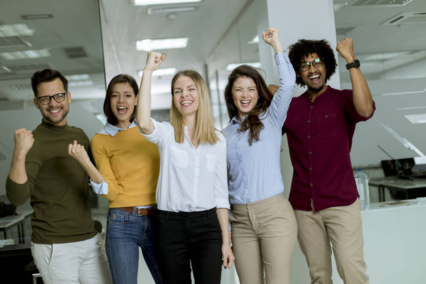 Portrait of group of young excited business people with hands up standing in office - 写真・画像