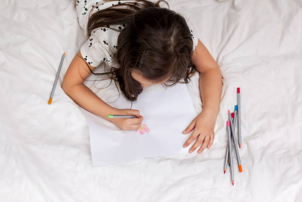 little girl drawing pictures while lying on bed. - 写真・画像