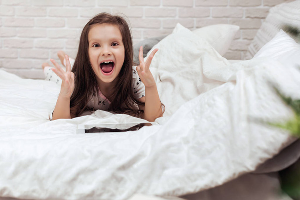 little child girl lies in bed uses digital tablet. - Foto, Imagen