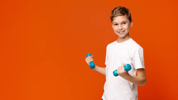Веселый мальчик тренируется с гантелями, оранжевый фон
 - Фото, изображение
