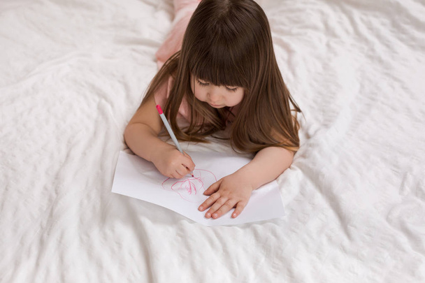 little girl drawing pictures while lying on bed. - Foto, Imagem