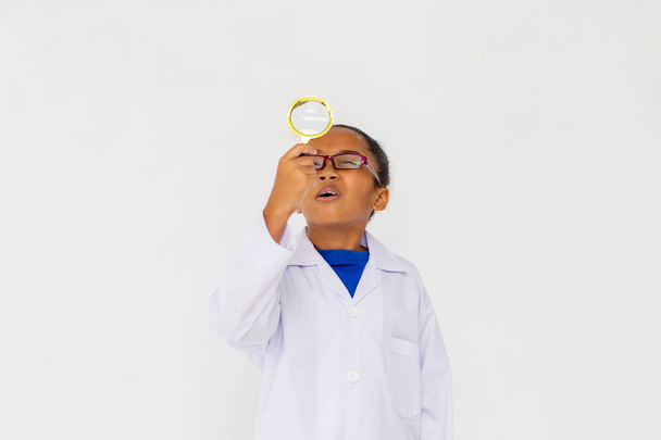 Young preteen African American kid wearing lab coat looking up with magnifier - Fotó, kép