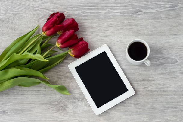 White tablet with a cup of coffee and red flowers lies on a whit - Foto, Imagem