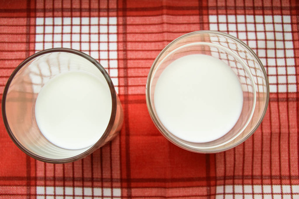 Deux verres de lait debout sur un tissu à carreaux rouges, vue de dessus
 - Photo, image