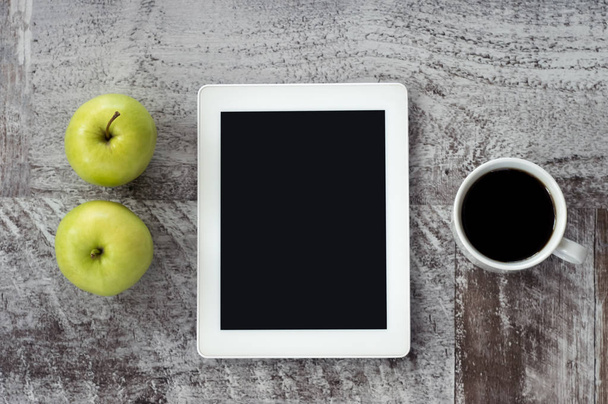 A white tablet with a cup of coffee and green apples lies on the - 写真・画像
