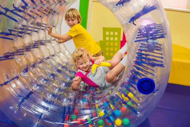 Cute little boy and girl playing in Zorb a rolling plastic cylinder ring with a hole in the middle, intdoor - Photo, image