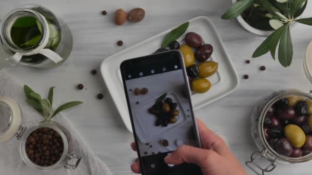 Smartphone in der Hand und fotografiert Oliven, Gewürze und Olivenöl. - Filmmaterial, Video