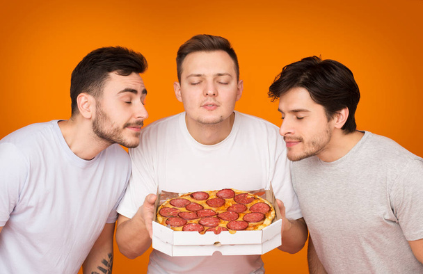 Trzy mężczyźni pachnące gorąca Pizza na pomarańczowe tło - Zdjęcie, obraz