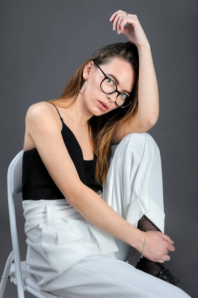 mudromá dívka v brýlích, sedí na židli na šedém pozadí - Fotografie, Obrázek