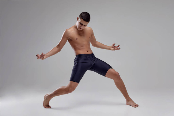 Photo of a handsome man ballet dancer, dressed in a black shorts, making a dance element against a gray background in studio. - Photo, Image