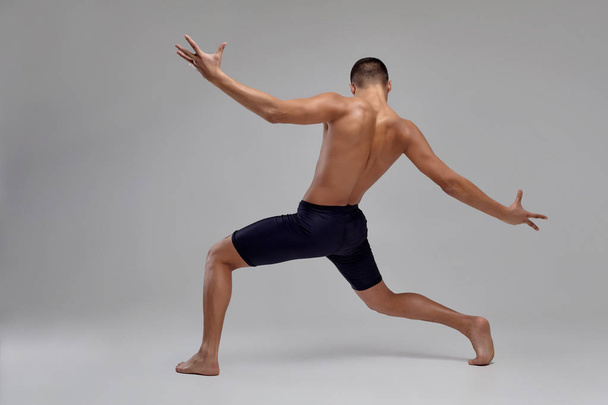 Foto de um homem bonito bailarino de balé, vestido com shorts pretos, fazendo um elemento de dança contra um fundo cinza no estúdio
. - Foto, Imagem