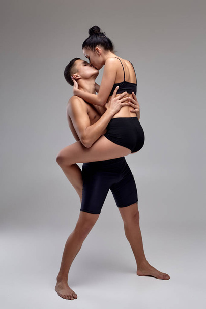 das Paar einer jungen modernen Balletttänzerin in schwarzen Anzügen posiert vor grauem Studiohintergrund. - Foto, Bild