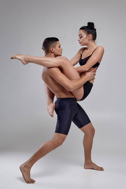 The couple of a young modern ballet dancers in black suits are posing over a gray studio background. - Foto, afbeelding