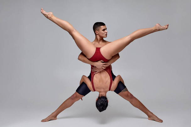 The couple of an athletic modern ballet dancers are posing against a gray studio background. - Foto, immagini
