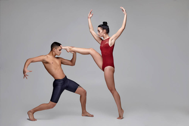 Το ζευγάρι των αθλητικών σύγχρονων χορευτών μπαλέτου ποζάρει σε ένα γκρίζο φόντο στούντιο. - Φωτογραφία, εικόνα