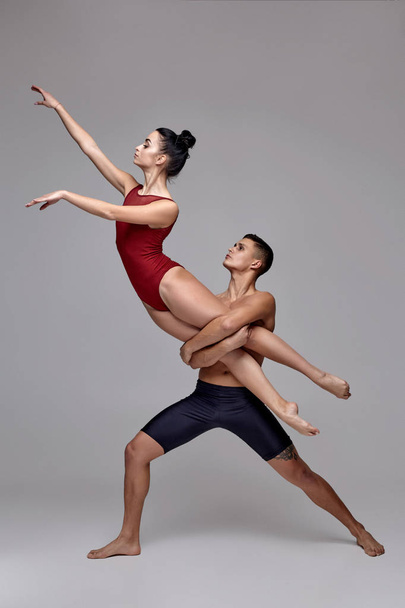 The couple of an athletic modern ballet dancers are posing against a gray studio background. - Photo, Image