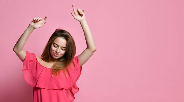 brunette girl dancing against pink wall with smile, rejoicing good mood. Student female  having fun while dancing to some pleasant music indoors - Фото, изображение