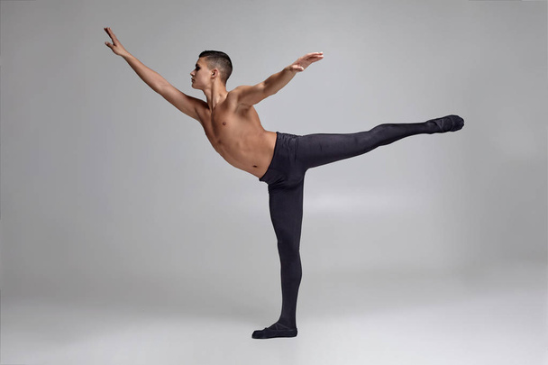 Bir atletik adam bale dansçısı Fotoğraf, siyah bir tayt ve pointe giymiş, stüdyoda gri bir arka plan karşı bir dans unsuru yapma. - Fotoğraf, Görsel