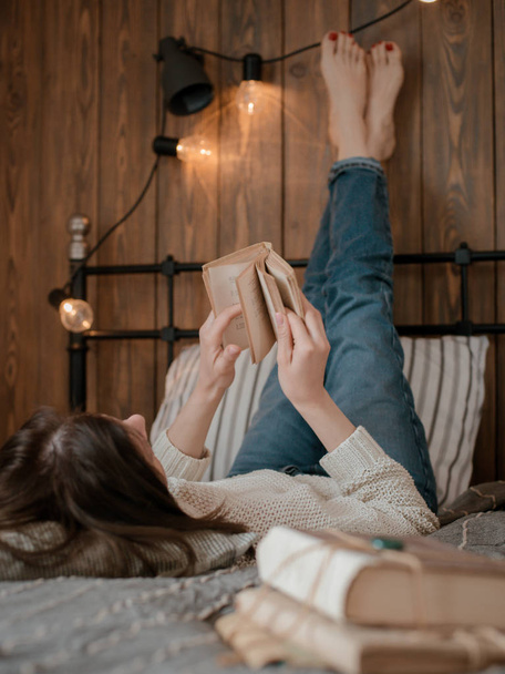 κορίτσι διαβάζοντας ένα βιβλίο και πίνοντας καφέ στο κρεβάτι πόδια στον τοίχο. - Φωτογραφία, εικόνα