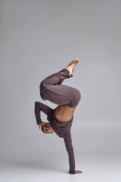 Foto di un ballerino atletico vestito con una tuta da ginnastica grigia, che fa un elemento di danza su uno sfondo grigio in studio
. - Foto, immagini