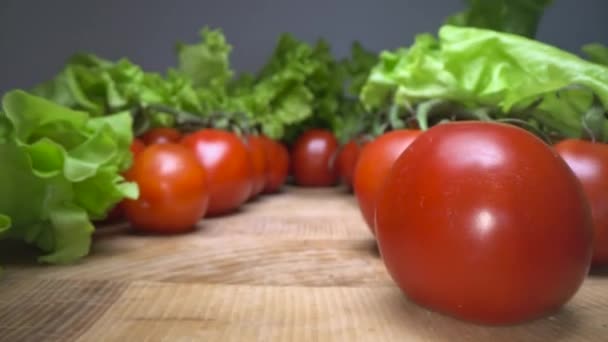 Dolly Schuss von roten fröhlichen Tomaten mit Salatblättern auf der Oberseite des hölzernen Tischhintergrunds. Gleiten durch heimisches Gemüse, gesunder Lebensstil - Filmmaterial, Video