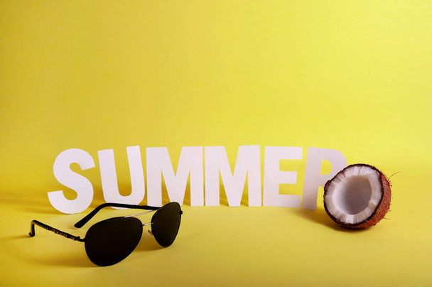 Word SUMMER made White Paper Letters with Half Coconut and glasses on Yellow Background. Copy Space For Your Text - Photo, Image