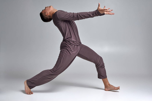 Photo d'un danseur de ballet homme athlétique vêtu d'un survêtement gris, faisant un élément de danse sur un fond gris en studio
. - Photo, image