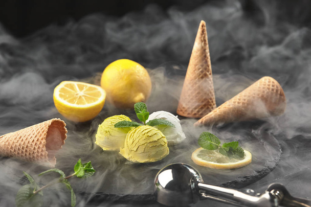 Вкусное сливочное и лимонное мороженое, украшенное мятой, подаваемое в дыму на каменной доске на черном фоне
. - Фото, изображение