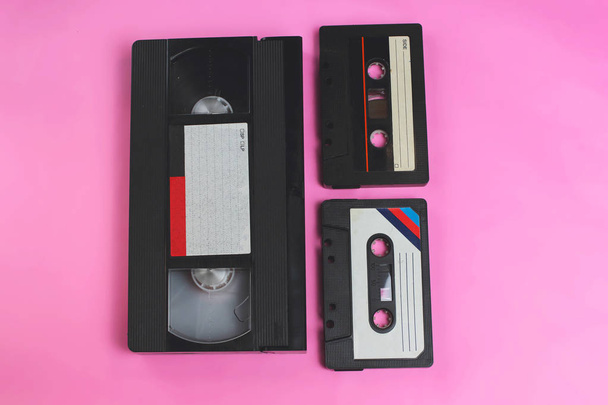 Ταινία βίντεο βιντεοκασέτα και κασέτα ήχου ρετρό vintage πνεύμα της δεκαετίας του 1970, δεκαετία του 1980, 1990 στυλ σε ροζ φόντο με επιλεκτική εστίαση - Φωτογραφία, εικόνα