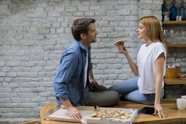 Νεαρό ζευγάρι στην αγάπη τρώει πίτσα για τον λαιμό στο ρουστίκ σπίτι - Φωτογραφία, εικόνα