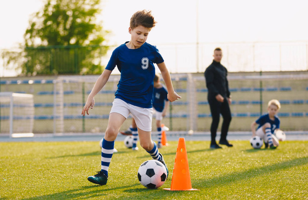 Τα αγόρια εκπαιδεύον ποδόσφαιρο να ντρίμπλάρει σε χωράφι. Παιδιά που τρέχουν την μπάλα. Οι παίκτες αναπτύσσουν δεξιότητες ντρίμπλων ποδοσφαίρου - Φωτογραφία, εικόνα