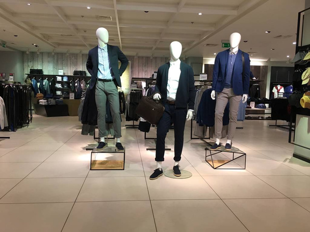 Tres maniquíes de hombres vestidos con ropa casual están de pie en la sala con vitrinas y estantes de una tienda de ropa
. - Foto, Imagen