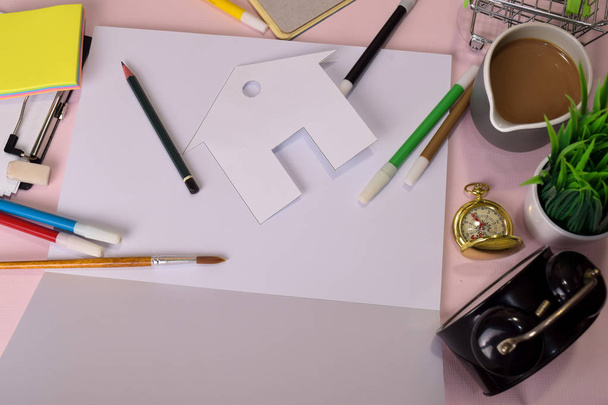 Vista superior del papel de corte o de la casa de dibujo sobre una mesa rosa, preparándose para hacer la tarea en un cuaderno abierto. Concepto de escritorio de dibujo
. - Foto, Imagen