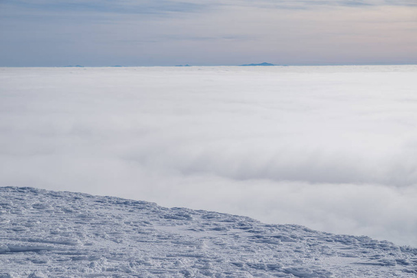 Mountain tops covered with snow above the white heavy clouds.  - 写真・画像