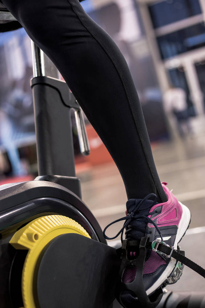 Primer plano de pie de niña en bicicleta deportiva negra y amarilla en el gimnasio para el entrenamiento
. - Foto, Imagen