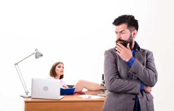 Занятой человек. Уверенный бизнесмен и симпатичная секретарша в офисе. Бородатый мужчина смотрит на сексуальную женщину, работающую на заднем плане. Жестокий кавказский мужчина с длинной бородой в деловой одежде с коллегой
 - Фото, изображение