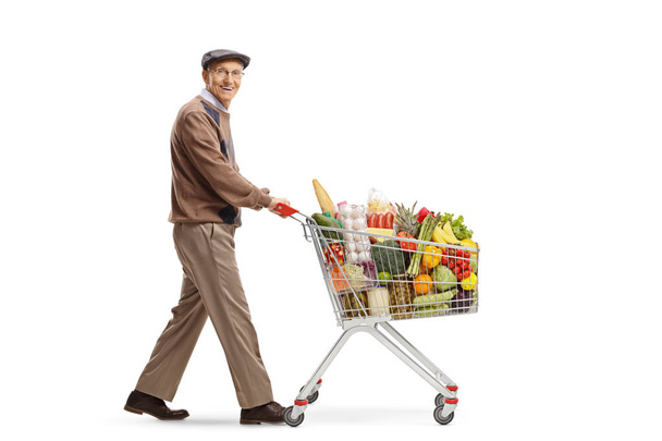 Full length shot of an elderly man pushing a shopping cart and looking at the camera isolated on white background - 写真・画像