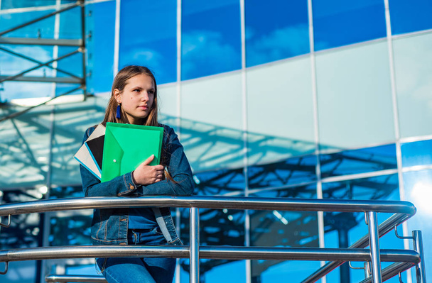 Back to school student teenager girl holding books and note books. Outdoor portrait of young teenager brunette girl with long hair. Glass building on background - Zdjęcie, obraz