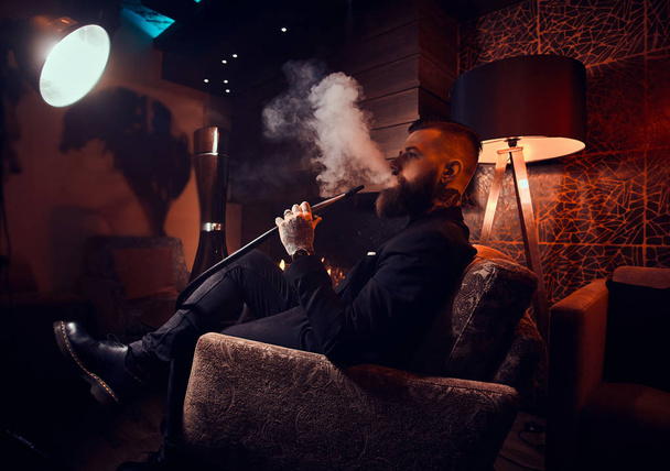 Elegant smart man is relaxing and smoking hookah after long hard day - Φωτογραφία, εικόνα