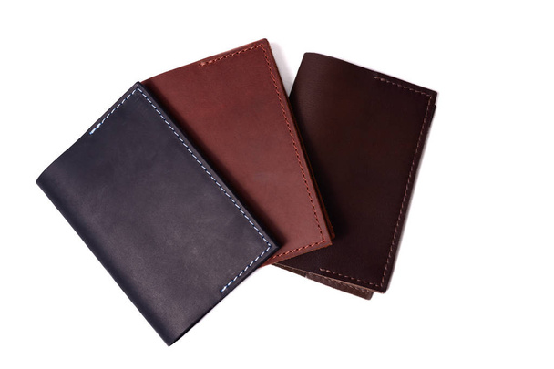 Three handmade leather passport covers isolated on white background. Closeup view. Covers are dark blue, red, brown and closed.  - Photo, Image