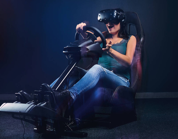 Młoda kobieta w Vr słuchawki zabawy podczas jazdy na samochód wyścigowy symulator kokpitu z siedzenia i koła. - Zdjęcie, obraz