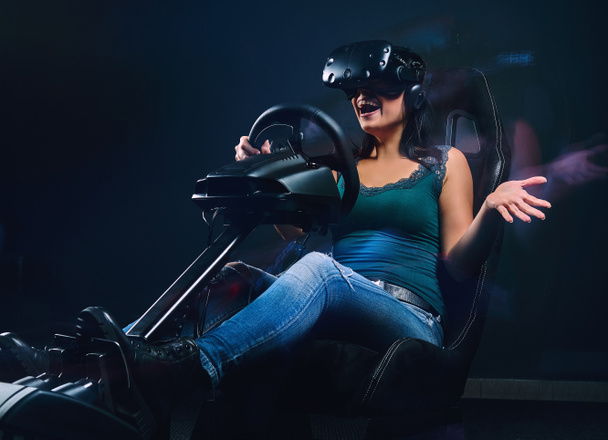 Young woman wearing VR headset having fun while driving on car racing simulator cockpit with seat and wheel. - 写真・画像