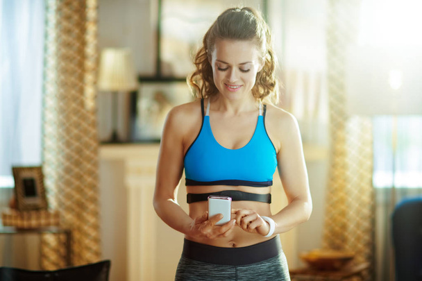 woman wearing heart rate monitor using fitness app in phone - Foto, imagen