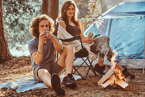 Couple of young students are chilling near bonfire in the green forest - Foto, Imagen