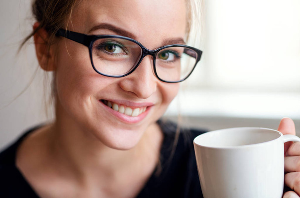 Bir fincan kahve tutan genç kız öğrencinin yakın çekim portresi. - Fotoğraf, Görsel
