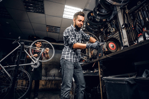 Atrakcyjny człowiek pracuje z maszyną w ruchliwym warsztacie rowerowym. - Zdjęcie, obraz