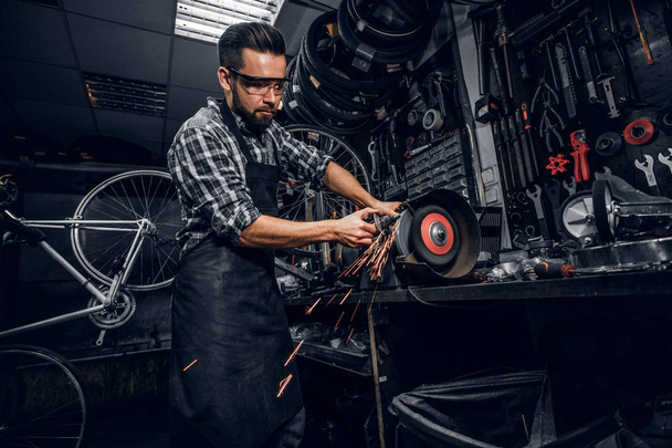Attractive man is working with machine at busy bicycle workshop. - Foto, afbeelding