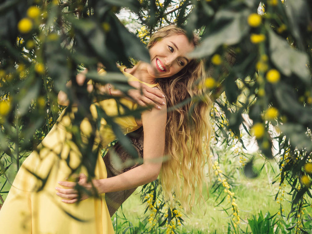 Young beautiful smiling woman in spring Australian Golden wattle trees. - Foto, immagini