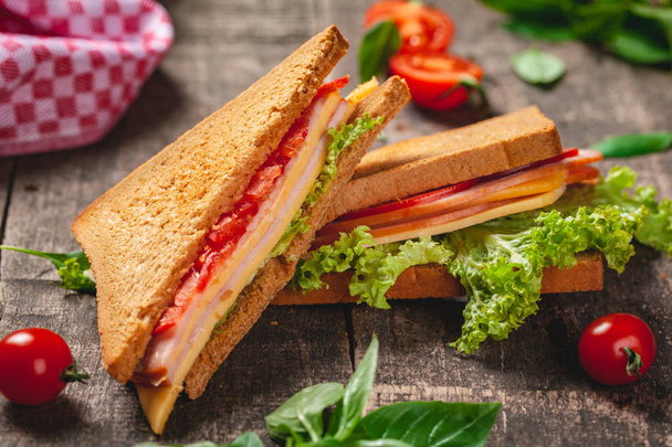 Sandwich with ham, cheese, tomatoes and lettuce leaves on wooden rustic table. Close up - Photo, Image